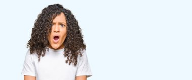 Kıvırcık saçlı genç güzel kadın beyaz t-shirt giyen şok yüzünde, şüpheci ve alaycı görünümlü, açık ağız ile şaşırttı