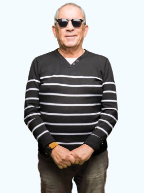 Yüzünde ciddi bir ifade ile kış kazak ve güneş gözlüğü giyen yakışıklı kıdemli adam. Basit ve doğal kamera bakıyor.