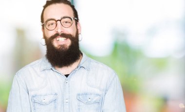 Genç hipster adam uzun saçlı ve gözlüklü eller birlikte sakal ve parmakları ile rahat ve neşeli gülümseyen geçti. Başarı ve iyimser