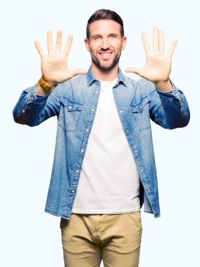 Mavi gözlü ve sakal gösteren ve parmak sayısı on ile işaret eden kot ceket giyen yakışıklı adam emin ve mutlu gülümseyen.