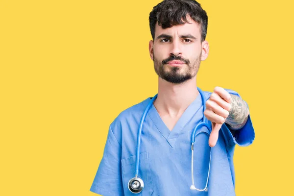 Young handsome nurse man wearing surgeon uniform over isolated background looking unhappy and angry showing rejection and negative with thumbs down gesture. Bad expression.