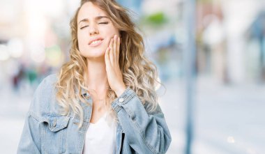 Diş ağrısı veya dişlerde dişlerle ilgili hastalık nedeniyle ağız acı ifadesi ile el ile dokunmak izole arka plan üzerinde kot ceket giyen güzel genç sarışın kadın. Diş hekimi kavramı.