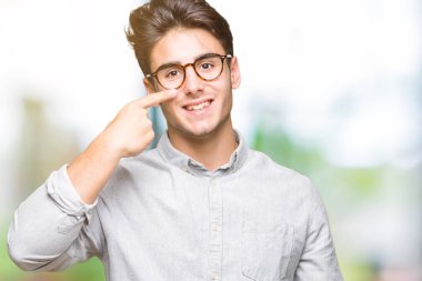 Genç yakışıklı adam gözlük izole üzerinde işaretleme için yüz ve burun, neşeli gülümseyerek el parmak ile arka plan