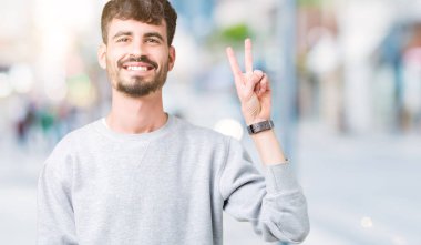 Gösterilen arka plan üzerinde sweatshirt giyen genç yakışıklı adam izole ve parmakları ile işaret kendinden emin ve mutlu gülümseyerek ise ikinci.