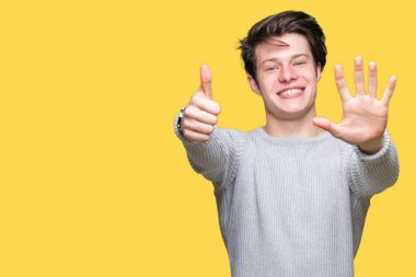 Gösterilen arka plan üzerinde kış kazak giyen genç yakışıklı adam izole ve parmakları ile işaret kendinden emin ve mutlu gülümseyerek süre 6 numara.