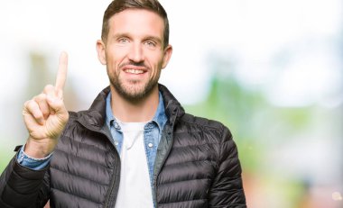 Yakışıklı adam kış ceket gösteren ve parmak numarası ile işaret giyen bir süre güven ve mutlu gülümseyen.