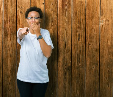 Güzel genç Afro-Amerikan kadın gözlük izole üzerinde gülme sizin parmak el kamerasıyla ağzına, utanç ifadesi işaret eden arka plan