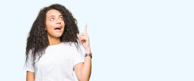 Casual beyaz t-shirt işaret parmağı ile başarılı fikir giyen kıvırcık saçlı Genç güzel kız. Çıktıktan ve mutlu. Bir numara.