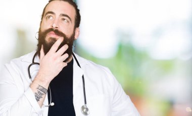 Doktor tıbbi ceket ve stetoskop el ile çene düşünme hakkında soru, dalgın ifade üzerine giymiş uzun saçlı. Düşünceli yüzüyle gülümsüyor. Şüphe kavramı.