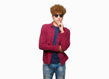 Yakışıklı genç afro saçlı çene düşünme hakkında soru, dalgın ifade üzerine el ile güneş gözlüğü takıyor. Düşünceli yüzüyle gülümsüyor. Şüphe kavramı.