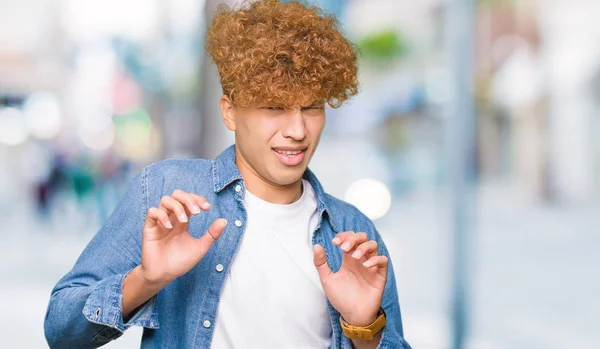 Young handsome man with afro hair wearing denim jacket disgusted expression, displeased and fearful doing disgust face because aversion reaction. With hands raised. Annoying concept.