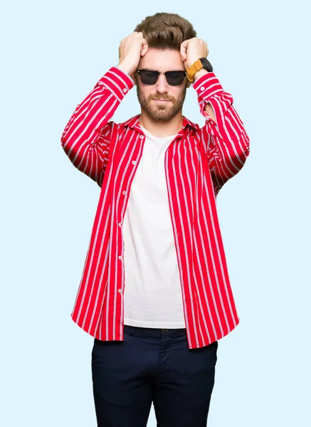 Yakışıklı delikanlı giyen güneş gözlüğü çünkü umutsuz ve stresli baş ağrısı acı acı ve migren. Ellerini kafasına.