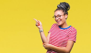 Kameraya bakarak yan el ve parmak ile işaret yüzünde kocaman bir gülümseme ile izole arka plan üzerinde gözlük takan saç Afro-Amerikan kız Genç örgülü.