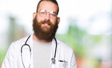 Genç Sarışın Doktor adam tıbbi kat eller birlikte giyen sakal ve parmakları ile rahat ve neşeli gülümseyen geçti. Başarı ve iyimser