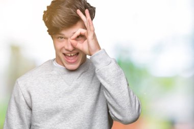 Genç yakışıklı sportif adam gülümsüyor, parmakları ile mutlu yüz üzerinden seyir göz el ile ok jest yapıyor izole arka plan üzerinde Sweatshirt giyiyor.