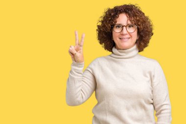 Boğazlı kazak ve gözlük ve parmak ikinci ile gülümseyen ise kendinden emin ve mutlu yukarıyı gösteren izole arka plan üzerinde giyen güzel orta ager üst düzey kadın.