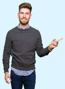 Yüzünde kocaman bir gülümseme ile genç yakışıklı zarif adam kameraya bakarak yan el ve parmak ile işaret.