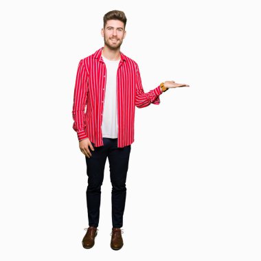 Kırmızı gömlek giyen genç yakışıklı adam neşeli sunan gülümseyerek ve kameraya bakarak avuç içi ile işaret.