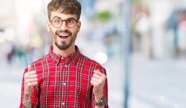 Yakışıklı delikanlı izole arka plan üzerinde kutluyor gözlük takan şaşırttı ve başarı için kaldırdı kollarını açarak hayret ve gözleri açık. Kazanan kavramı.