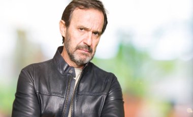 Orta Çağ yakışıklı adam siyah deri ceket giyerek şüpheci ve sinir, kesişmiş kollar ile yüz üzerine ifade onaylamıyor. Negatif kişi.