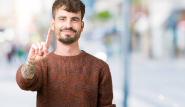 Genç yakışıklı adam giyen kış kazak izole üzerinde arka plan işaret parmağını ve kızgın ifade ile