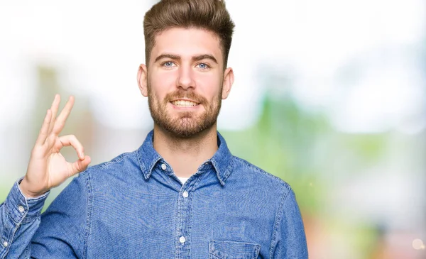 El ve parmak ile ok işareti yapıyor olumlu gülümseyen rahat kot gömlek giymiş genç yakışıklı sarışın adam. Başarılı ifade.