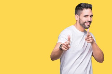 Fotoğraf makinesi ile mutlu ve komik yüz için parmakları işaret izole arka plan üzerinde rahat beyaz t-shirt giyen genç adam. İyi enerji ve vibes.