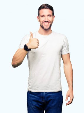 Yakışıklı adam hareketi el ile mutlu yaşasın yaparken rahat beyaz t-shirt giyiyor. Başarı gösteren kameraya bakarak ifade onaylama.