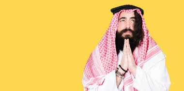 Uzun saçlı geleneksel Puşi eşarp giyen Arap iş adamı yalvarıyor ve el ile birlikte dua yüz üzerinde umut ifade ile çok duygusal ve endişeli. Affedilmesini istiyorum. Din konsepti.