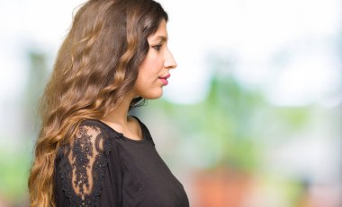 Yan bakan uzun saçlı güzel genç kadın, kendine güvenen gülümseme ile doğal yüzü ile profil poz dinlenmek.