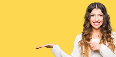 Hayret ve el ile sunulması ve parmak ile işaret ederken kameraya gülümseyen beyaz kazak giyen genç güzel kadın.