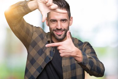 Yakışıklı delikanlı elle yapma çerçeve ve parmakları ile mutlu yüz gülümseyen izole arka plan üzerinde. Yaratıcılık ve Fotoğrafçılık kavramı.