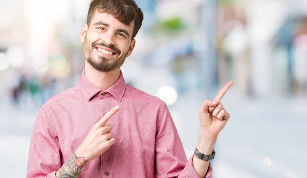 年轻英俊的男人穿着粉红色的衬衫在孤立的背景微笑着 看着相机指向镜头 用两只手和手指指着一边 — 图库照片