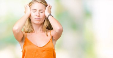 Çünkü çaresiz ve stresli baş ağrısı acı izole arka plan üzerinde turuncu gömlek giymiş güzel genç kadın acı ve migren. Ellerini kafasına.