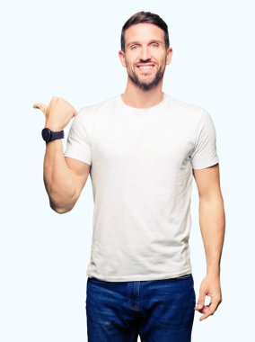 Casual beyaz t-shirt arıyorsunuz ve başparmak yanında yukarıyı mutlu yüz ile gülümseyen giyen yakışıklı adam.