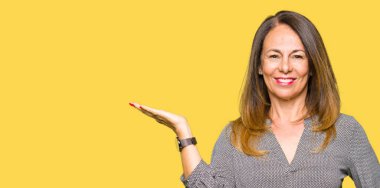 Güzel orta yaş iş kadın neşeli sunumu gülümseyen ve el kamera bakarak avuç ile işaret.