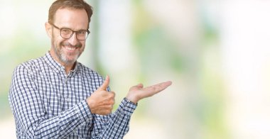 Arka plan gösteren palm el üzerinde gözlük takan yakışıklı orta yaş zarif komuta sizde izole ve mutlu ve neşeli gülümseyen thumbs up, ok hareketi ile yapıyor