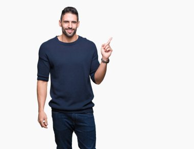 Yüz üzerinde büyük bir gülümseme ile izole arka plan üzerinde kazak giyen genç yakışıklı adam, kamera bakarak yan el ve parmak ile işaret.