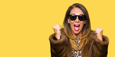 Güzel orta yaş zarif kadın giyiyor güneş gözlüğü ve vizon şaşırmış ve hayret için başarı ile silah kaldırdı kutluyor ceket ve gözleri açık. Kazanan kavramı.