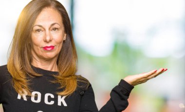 Güzel orta yaş kadın rock ve rulo kazak gülümseyen neşeli sunan ve kamera bakarak el avuç ile işaret giyiyor.