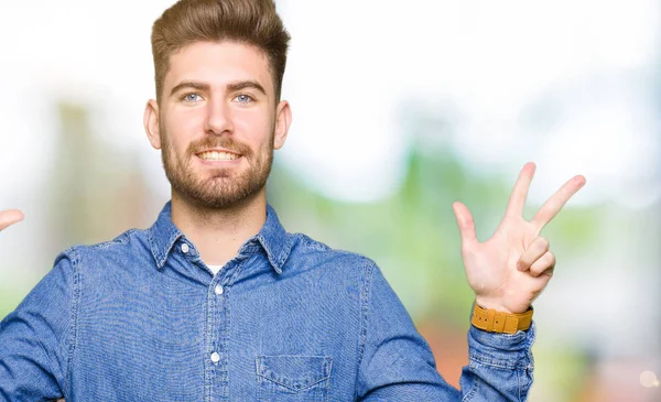 Young handsome blond man wearing casual denim shirt showing and pointing up with fingers number eight while smiling confident and happy.