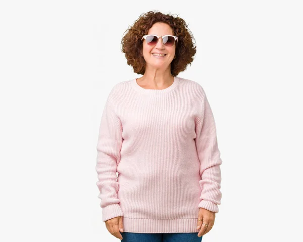 美しい中間エイガーの年配の女性の顔に幸せとクールな笑顔で孤立した背景にピンクのセーター サングラスを着用します 幸運な人 — ストック写真