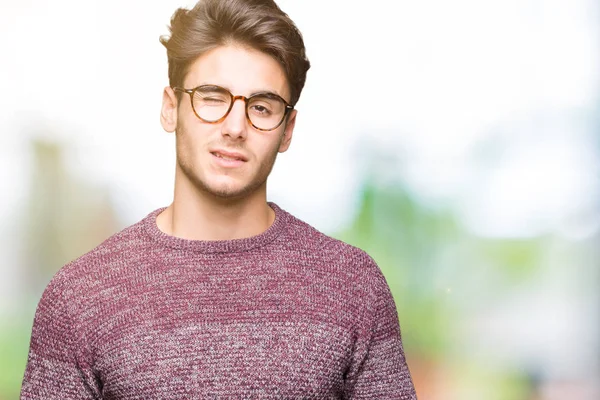 Seksi bir ifadeyle, neşeli ve mutlu yüzünü kameraya bakarak göz kırpıyor izole arka plan üzerinde gözlük takan genç yakışıklı adam.