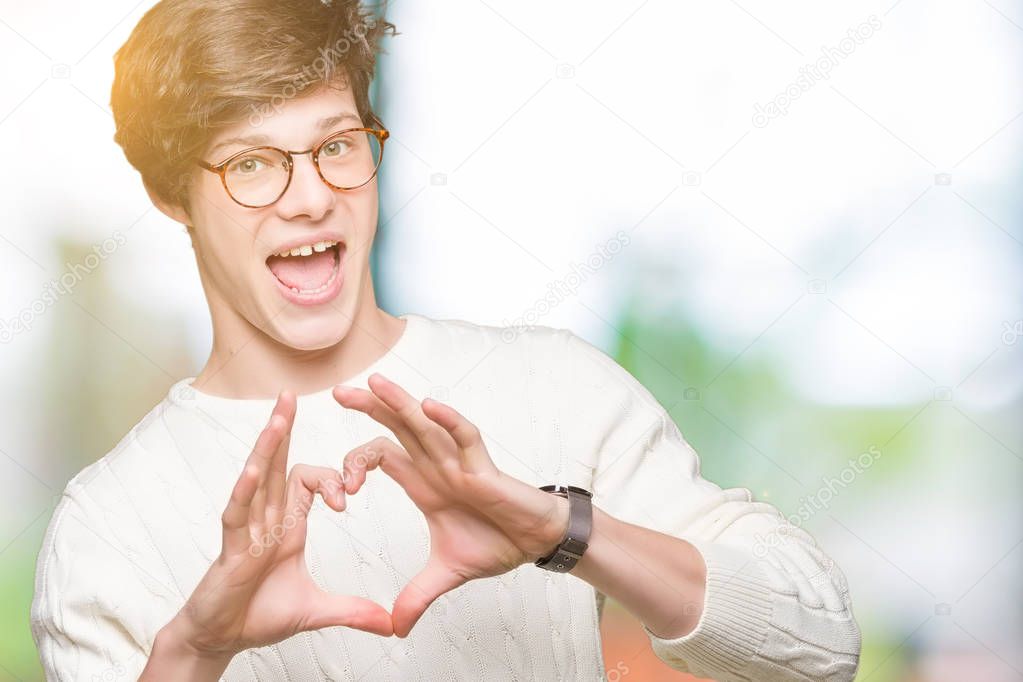 Young handsome man wearing glasses over isolated background smiling in love showing heart symbol and shape with hands. Romantic concept.