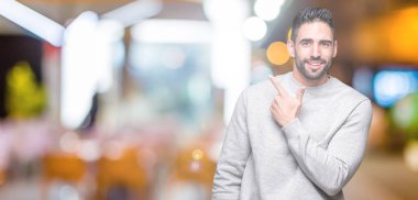 İzole arka neşeli bir gülümseme ile el ve parmak kadar yan yüzünde mutlu ve doğal ifade ile işaret yüz üzerinden sweatshirt giyen genç yakışıklı adam