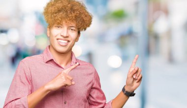 Gülümseyen ve iki elleri ve parmakları ile tarafına işaret kamera bakarak afro saçlı genç yakışıklı iş adamı.