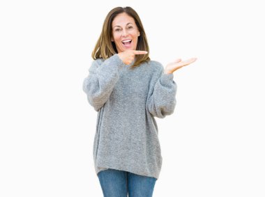 Hayret ve el ile sunulması ve parmak ile işaret ederken kameraya gülümseyen izole arka plan üzerinde kış kazak giyen güzel orta yaş kadın.