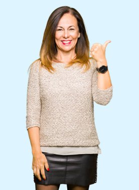 Seyir ve başparmak yanında yukarıyı mutlu yüz ile gülümseyen moda kazak giyen güzel orta yaş kadın.