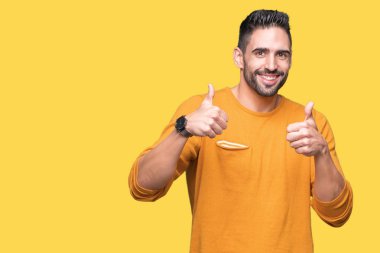 Yakışıklı delikanlı izole arka plan başarı işareti el ile pozitif jest yapıyor üzerinde başparmak gülümseyen ve mutlu. Neşeli bir ifadeyle, kazanan jest kameraya bakıyor.