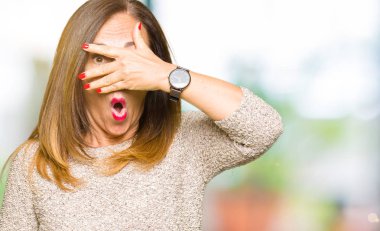 Moda kazak giyen güzel orta yaş kadın el ile yüz ve gözlerini kaplayan şok göz, utanmış ifade ile parmaklar bakarak.